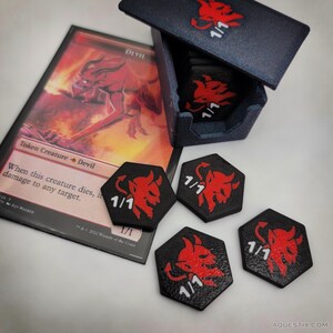 May include: A black box with a red devil logo and several black and red tokens with a devil graphic and "1/1" text. A card with a devil illustration and the text "Token Creature Devil" is also visible.