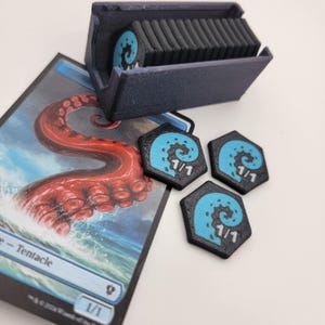 May include: A dark blue card holder with a stack of cards and three black and blue tokens. The tokens have a blue tentacle design and the numbers 1/1. A card with a red tentacle is also visible.