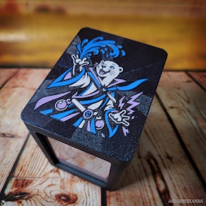 May include: A black rectangular box featuring a graphic of an otter wearing a robe and casting a spell with blue and purple accents. The otter is depicted with a splash of blue water above its head and lightning bolts on the side. Aquestix.com is printed.