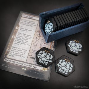 Op de afbeelding: Een set zwart-witte kaartspel tokens met een blauwe opbergdoos. De tokens hebben een wit en zwart ontwerp. De kaart leest "Urza's Saga". De tokens zijn zeshoekig en hebben een uniek ontwerp. De set is voor een kaartspel.