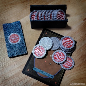 May include: A set of 15 silver and red bottle caps with the words "Nuka Cola" printed on them. The bottle caps are in a black box and on a card with the word "Deckmaster" printed on it.