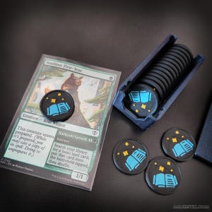 Könnte beinhalten: Schwarze, runde Spielmarken mit einem Design aus blauem Buch und Sternen, neben einer Karte mit der Aufschrift "Studious First-Year". Die Marken befinden sich in einem blauen Behälter, einige liegen lose herum.