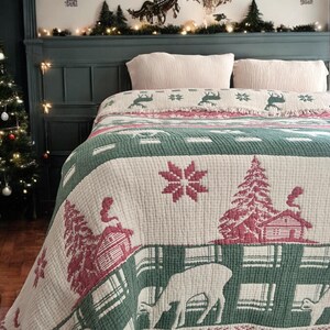 May include: A white and green throw blanket with a festive Christmas design. The blanket features red and white snowflakes, a red and white cabin, a green pine tree, and white deer. The blanket has a fringed edge.