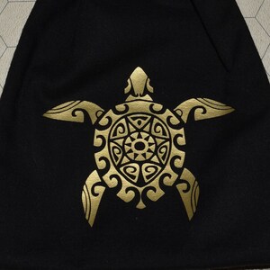 May include: A black drawstring bag with a gold turtle design. Assorted polyhedral dice of various colors are scattered around the bag. The bag is made of a soft material and has a drawstring closure.