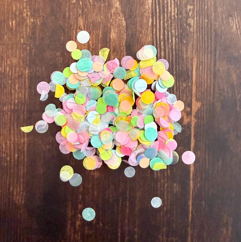 Op de afbeelding: Een stapel kleurrijke confetti in verschillende pastelkleuren, waaronder roze, geel, groen en blauw. De confetti is verspreid over een donkerbruin houten oppervlak, wat een feestelijke sfeer cre&euml;ert.