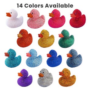 May include: A selection of fourteen decorative duck figurines in a range of colours, each covered in small, sparkling embellishments. The ducks have orange beaks and feet. The available colours include white, pink, red, orange, yellow, green, blue, and purple.
