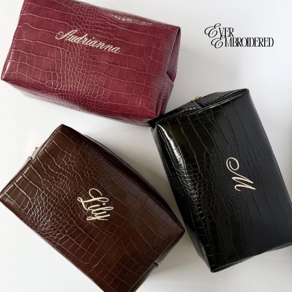May include: Three rectangular cosmetic bags with a crocodile-embossed texture in burgundy, brown, and black. Each bag features gold-colored embroidered personalization: Audrianna, Lily, and M. The text Ever Embroidered is visible in the top right corner.