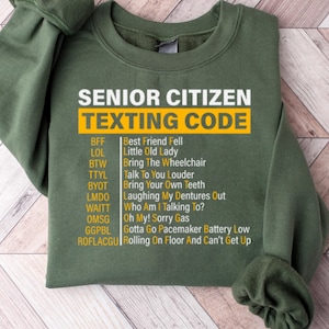 May include: Green sweatshirt with a white graphic print that says "Senior Citizen Texting Code" and lists common texting abbreviations and their meanings.
