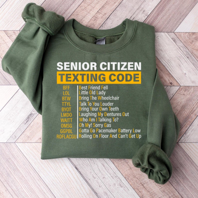 May include: Green sweatshirt with a white graphic print that says "Senior Citizen Texting Code" and lists common texting abbreviations and their meanings.