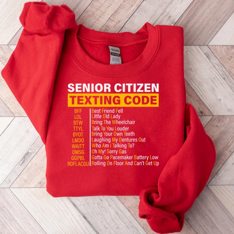 May include: Red sweatshirt with a yellow graphic that says "Senior Citizen Texting Code" and lists common texting abbreviations and their meanings.