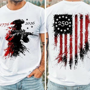 May include: A white t-shirt featuring a graphic print on the front and back. The front displays a silhouette of a soldier in a tricorn hat holding a rifle with the text 1776 and 2026. The back shows a distressed American flag with 250 in the center.