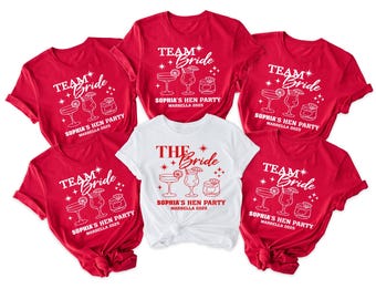 May include: A collection of red and white t-shirts with the text "TEAM Bride" and "THE Bride" in white and red, respectively. The shirts feature cocktail illustrations and the text "Sophia's Hen Party Marbella 2025".