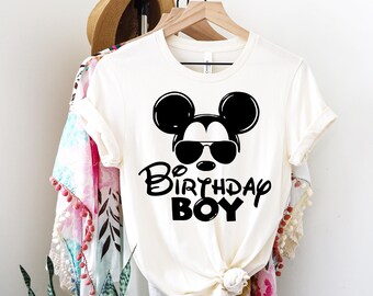 May include: White t-shirt with a black Mickey Mouse graphic wearing sunglasses and the text "Be Birthday Boy".
