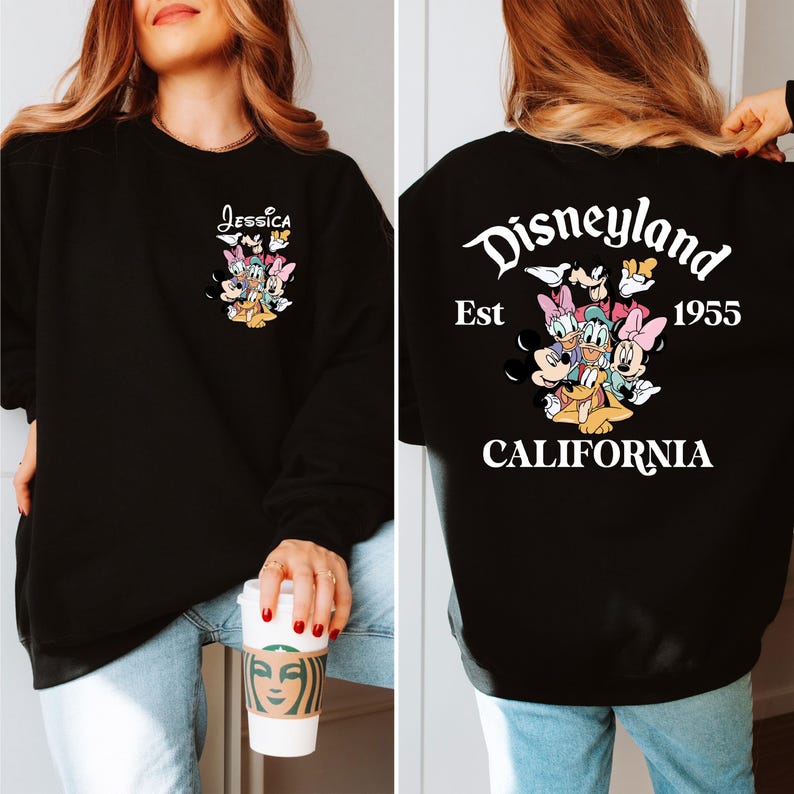 May include: Black sweatshirt featuring a colorful graphic of Disney characters. The front displays the name "Jessica" above the characters. The back of the sweatshirt has the Disneyland logo, the year "1955", and the word "CALIFORNIA".