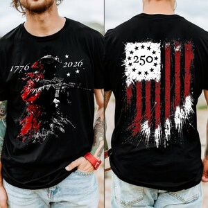 May include: A black t-shirt featuring a graphic on the front and back. The front displays a silhouette of a soldier with a rifle, the text 1776 and 2026, and stars. The back shows a distressed American flag design with the number 250 inside a circle.