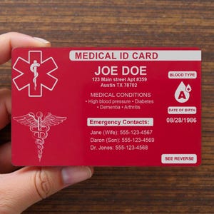 Könnte beinhalten: Eine rote medizinische ID-Karte mit weißem Text und Symbolen. Die Karte enthält den Namen "JOE DOE", die Adresse, medizinische Bedingungen, Notfallkontakte, Blutgruppe "A" und das Geburtsdatum. Sie zeigt ein medizinisches Symbol und ein Caduceus-Symbol.