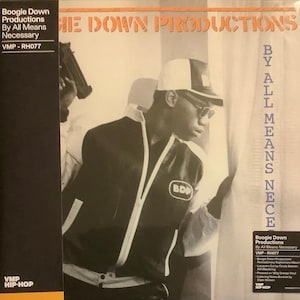 May include: A black and white photograph of a man wearing a black jacket with a white stripe and a white baseball cap. The jacket has a white BDP logo on the left side. The man is looking to the right. The background is a white wall with a white curtain. The text "Boogie Down Productions By All Means Necessary VMP-RH077" is printed on the right side of the image.