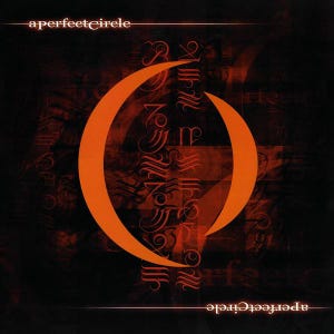 May include: A dark red and black album cover with the text "a perfect circle" in white. The album cover features a large, orange crescent moon shape.