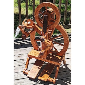 May include: A wooden spinning wheel with a large wheel and a smaller wheel, both with spokes. The spinning wheel is on a wooden stand with two pedals. The spinning wheel is made of cherry wood and has a natural finish.