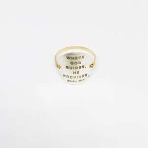 Puede incluir: Un anillo de plata con una banda de oro y un colgante en forma de coraz&oacute;n. El colgante tiene las palabras "Where God Guides, He Provides. Isaiah 58:11" grabadas.