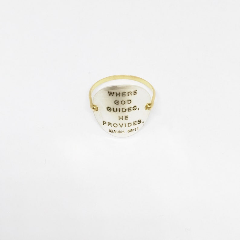 Puede incluir: Un anillo de plata con una banda de oro y un colgante en forma de coraz&oacute;n. El colgante tiene las palabras "Where God Guides, He Provides. Isaiah 58:11" grabadas.