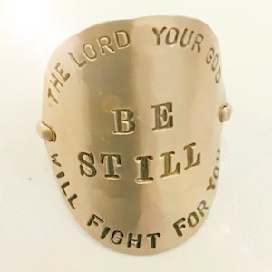 May include: A gold-toned metal ring with the words "The Lord Your God Will Fight For You" and "Be Still" engraved on it.