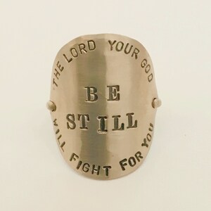 May include: A silver ring with the words "The Lord Your God Will Fight For You" and "Be Still" engraved on it.
