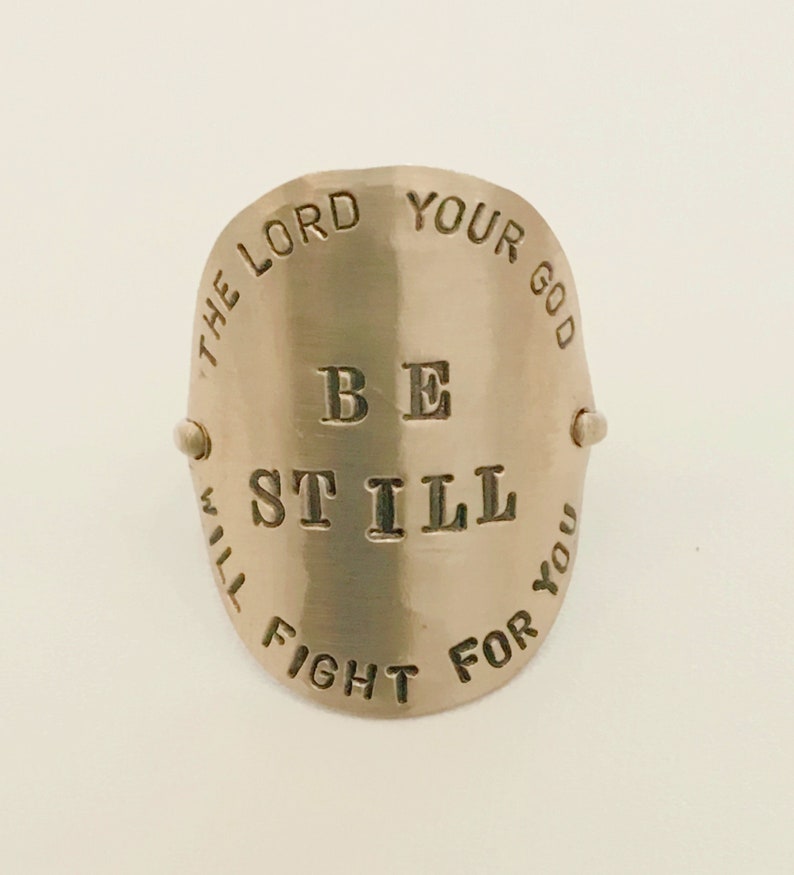 May include: A silver ring with the words "The Lord Your God Will Fight For You" and "Be Still" engraved on it.