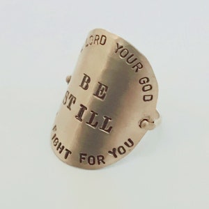 May include: A silver ring with the words "Be Still" and "Your God Will Fight For You" engraved on it.