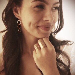 May include: A woman wearing gold hoop earrings and a gold ring with the inscription "Be the change you wish to see in the world".