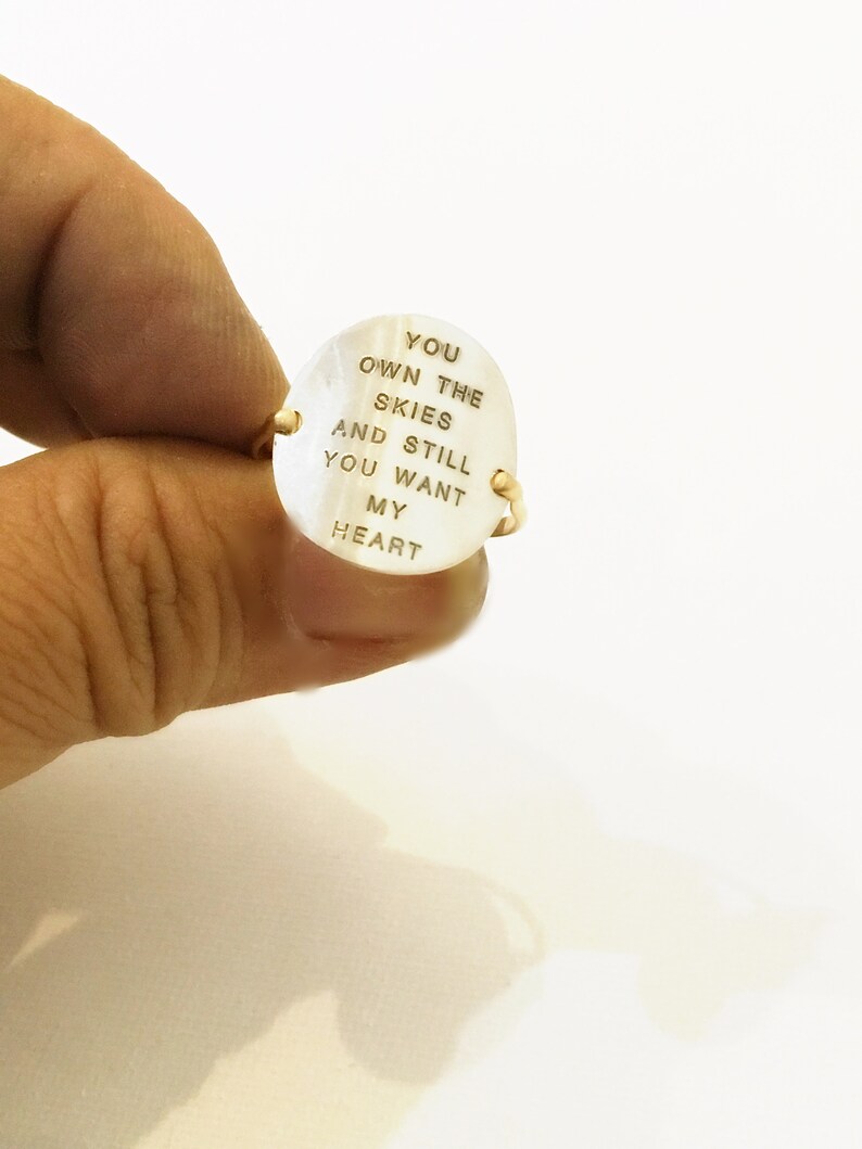 Pu&ograve; includere: Un anello d'oro con una pietra ovale bianca. La pietra &egrave; incisa con le parole "You own the skies and still you want my heart".