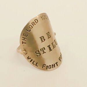 May include: Gold-toned ring with the words "Be Still The Lord Your Will Fight For You" engraved on it.