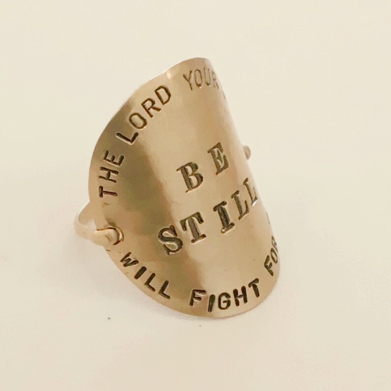 May include: Gold-toned ring with the words "Be Still The Lord Your Will Fight For You" engraved on it.
