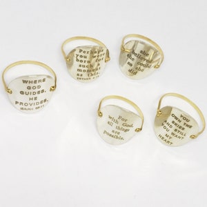 Puede incluir: Cuatro anillos de oro con medallones redondos de plata grabados con citas inspiradoras. Las citas son: "Donde Dios gu&iacute;a, &Eacute;l provee. Isa&iacute;as 58:11", "Tal vez naciste para un momento como este. Ester 4:18", "Ella cre&iacute;a que pod&iacute;a, as&iacute; que lo hizo", y "Porque con Dios, todo es posible."