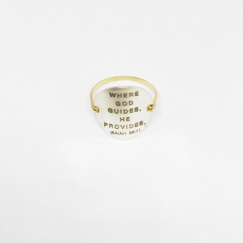 Puede incluir: Un anillo de oro con un dije ovalado de plata que dice "Where God Guides, He Provides. Isaiah 58:11"