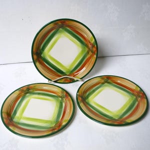 May include: Three ceramic plates with a green, orange, and brown geometric design. The plates have a white center with a diamond shape outlined in green.