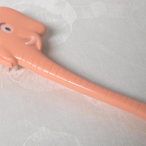 May include: A pink plastic brush with an elephant head design. The brush has white bristles and a long handle.