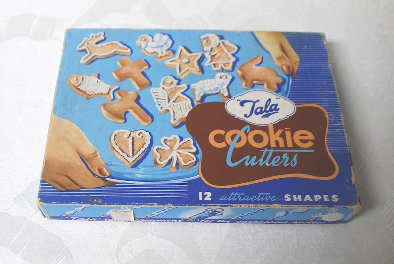 Puede incluir: Una caja azul y marr&oacute;n con el texto "Tala Cookie Cutters" y "12 formas atractivas". La caja contiene 12 cortadores de galletas en varias formas, incluyendo un pez, una cruz, un coraz&oacute;n, un tr&eacute;bol de cuatro hojas, una estrella, un cordero, un conejo, un p&aacute;jaro y un reno.