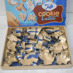 Puede incluir: Una caja vintage de cortadores de galletas Tala en una caja azul y blanca con el texto "Tala Cookie Cutters". La caja est&aacute; abierta y los cortadores de galletas est&aacute;n dispuestos en el interior. Los cortadores de galletas son de metal y tienen varias formas, incluyendo estrellas, corazones y animales.