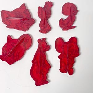May include: Six red plastic cookie cutters in various animal shapes, including a pig, rooster, duck, bear, and mouse. The cutters are transparent and have a slot for easy use. Ideal for baking themed cookies.