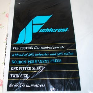 May include: A white package with a black and gold label. The label says "Fieldcrest Perfection fine combed percale a blend of 50% polyester and 50% cotton NO IRON PERMANENT PRESS ONE FITTED SHEET TWIN SIZE for 39 X 75 in. mattress"