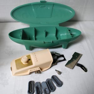 May include: Vintage Singer sewing machine with accessories. The machine is cream-colored with gold accents and the word "SINGER" printed on the side. Includes a teal carrying case, presser feet, and other attachments. A classic sewing machine.