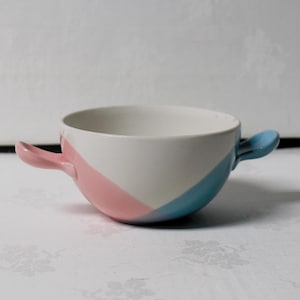 May include: A ceramic soup bowl with two handles. The bowl is white with a diagonal stripe of pink on one side and a diagonal stripe of blue on the other. The handles are pink and blue.