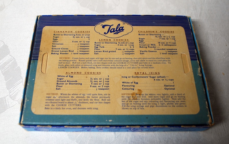 Puede incluir: Una caja vintage de cortadores de galletas "Tala" con recetas para galletas de canela, lim&oacute;n, para ni&ntilde;os, de almendras y glaseado real. La caja es azul y blanca con un inserto de cart&oacute;n marr&oacute;n.