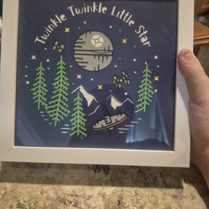Può includere: Stampa artistica con cornice bianca con sfondo blu navy con il testo "Twinkle Twinkle Little Star". La stampa include illustrazioni di una Morte Nera, astronavi, montagne, alberi e stelle.