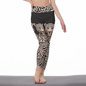 May include: Black leggings with a leopard print design. The leggings have a high waistband with a leopard print pattern and a black panel with two leopard faces. The lower legs have a white and brown animal print.