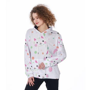 Könnte beinhalten: Weißer Kapuzenpullover mit einem Katzenmuster, mit rosa, grünen und orangefarbenen Akzenten. Das Design umfasst Katzenköpfe, Punkte und geometrische Formen. Der Hoodie hat eine Vordertasche und eine Kapuze mit Kordelzug.