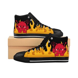 May include: Black high-top sneakers featuring a cartoon devil design. The shoes have a black toe cap, laces, and ankle, with a yellow flame pattern and a red devil character holding a trident. The soles are black with a white stripe.