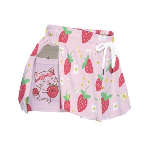 Könnte beinhalten: Hellrosa Rock mit Erdbeermuster und weißem Kordelzug. Der Rock hat eine Tasche mit einer Cartoon-Katze, die eine Erdbeere hält. Die Erdbeeren sind rot mit grünen Blättern, und die Blumen sind weiß und gelb.