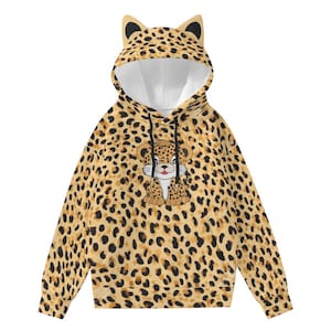Pode incluir: Um moletom com capuz com estampa de leopardo. O moletom apresenta um desenho de leopardo de desenho animado na frente e orelhas de gato no capuz. É principalmente bege com manchas pretas.